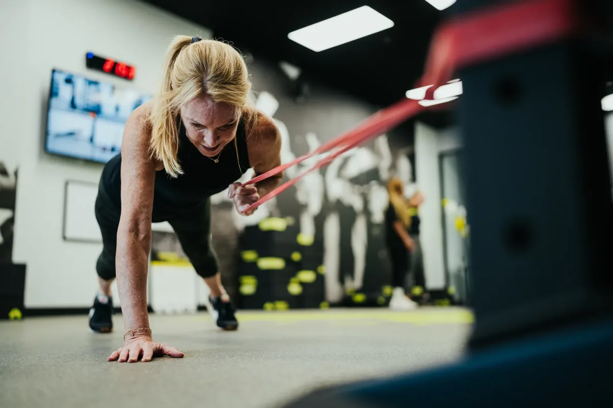 A woman works through a banded plank row on the studio floor during a training session