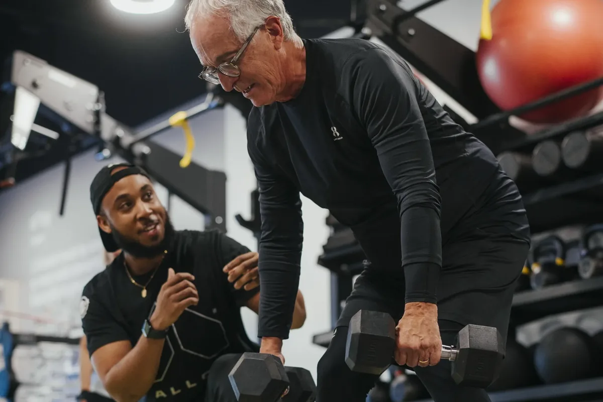 A coach encourages an older member mid set of dumbbell rows