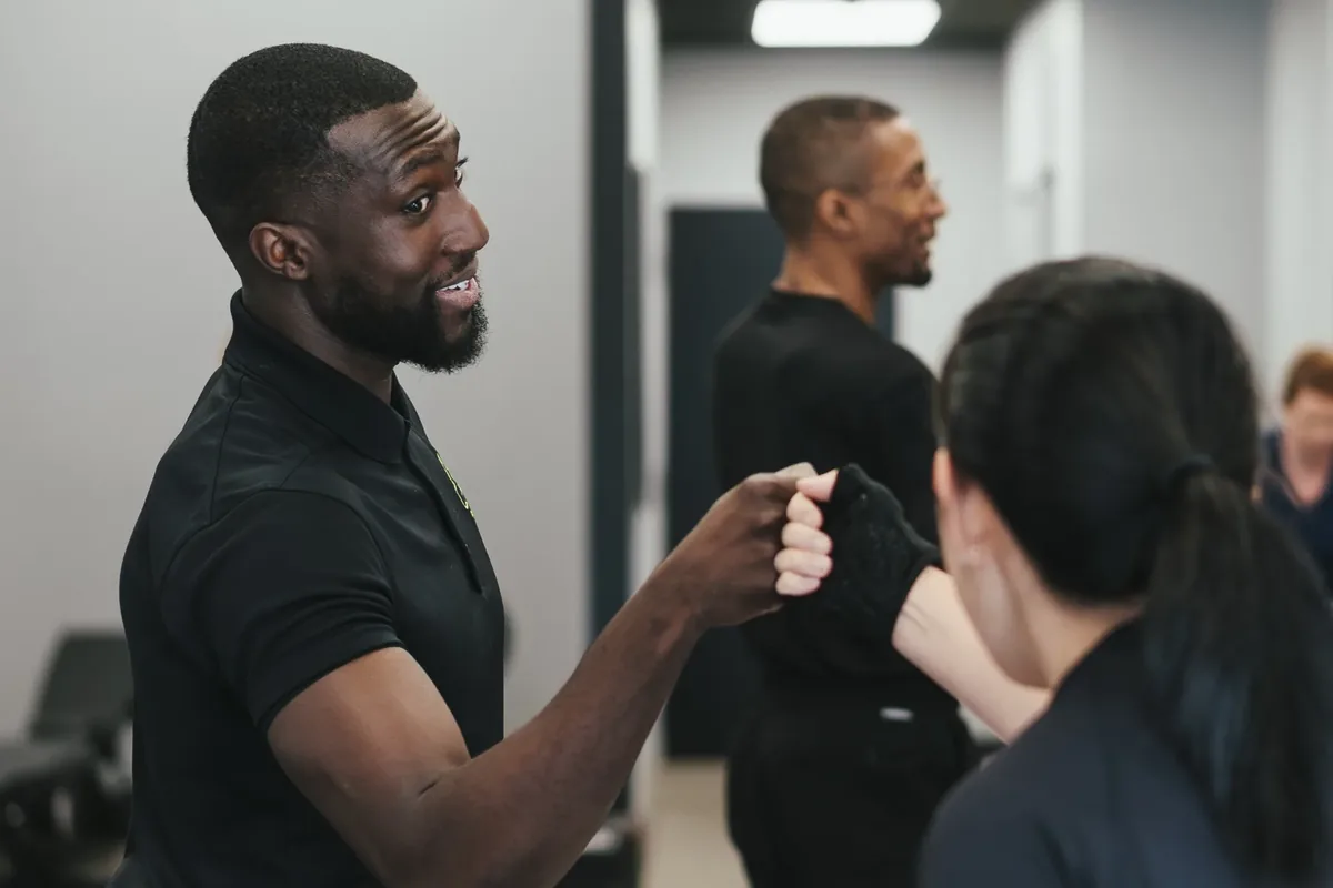 A trainer fist-bumps a member with other members training in the background