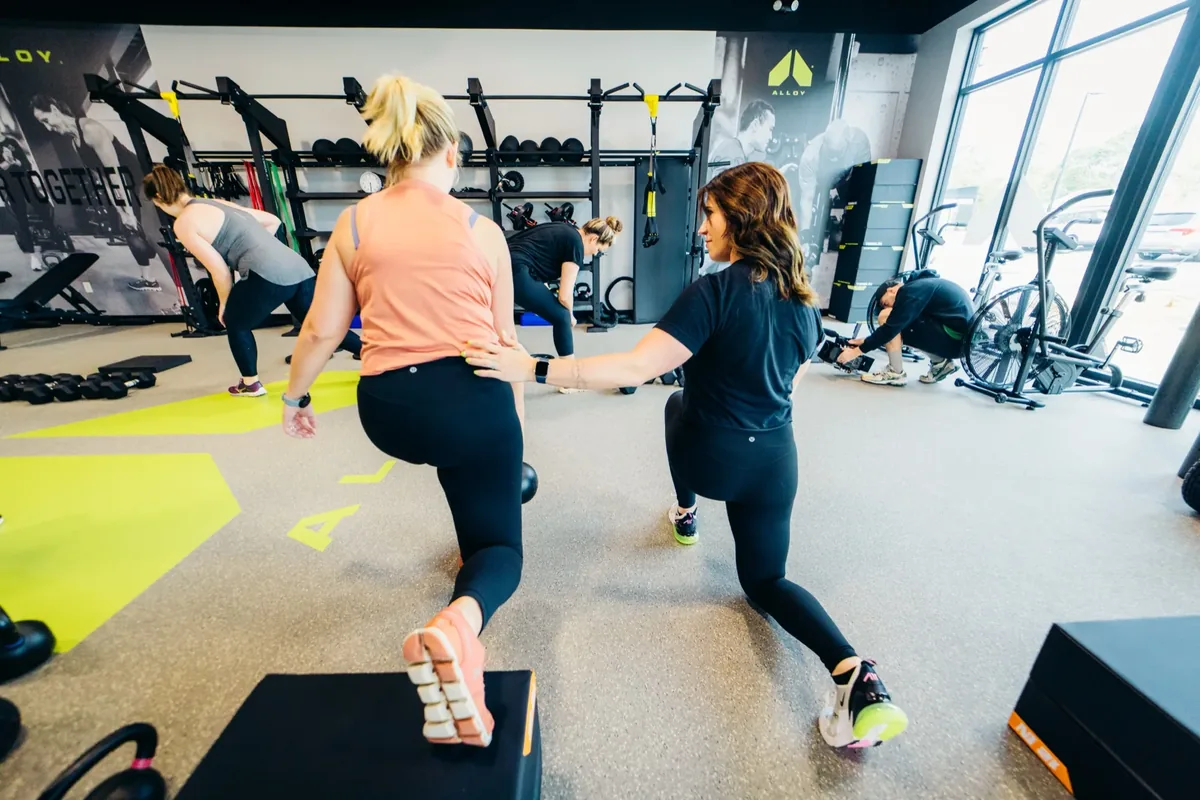 Trainer adjusts a member's form during a small group session at Alloy Personal Training — Billings, MT